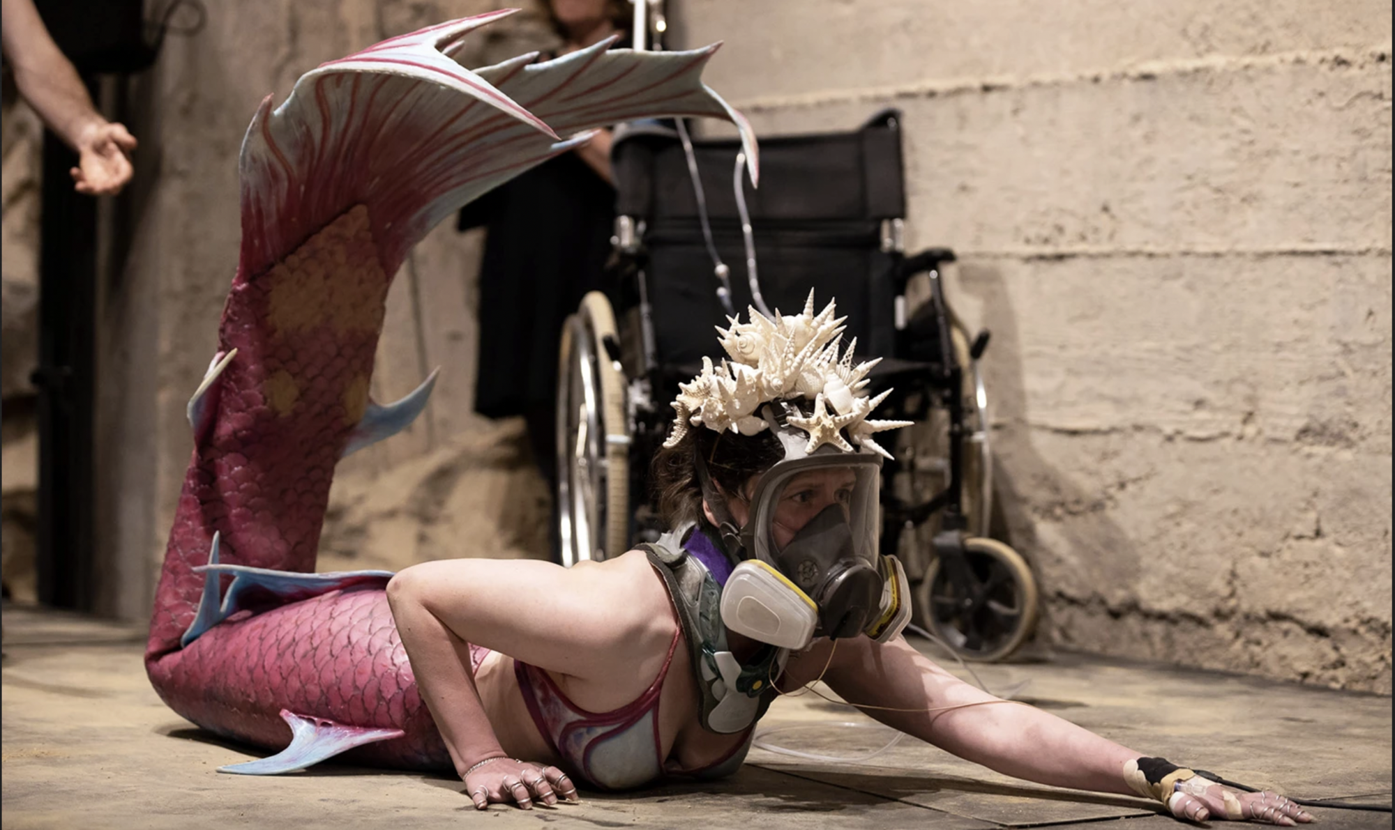 A person dressed like a mermaid crawls on the floor.