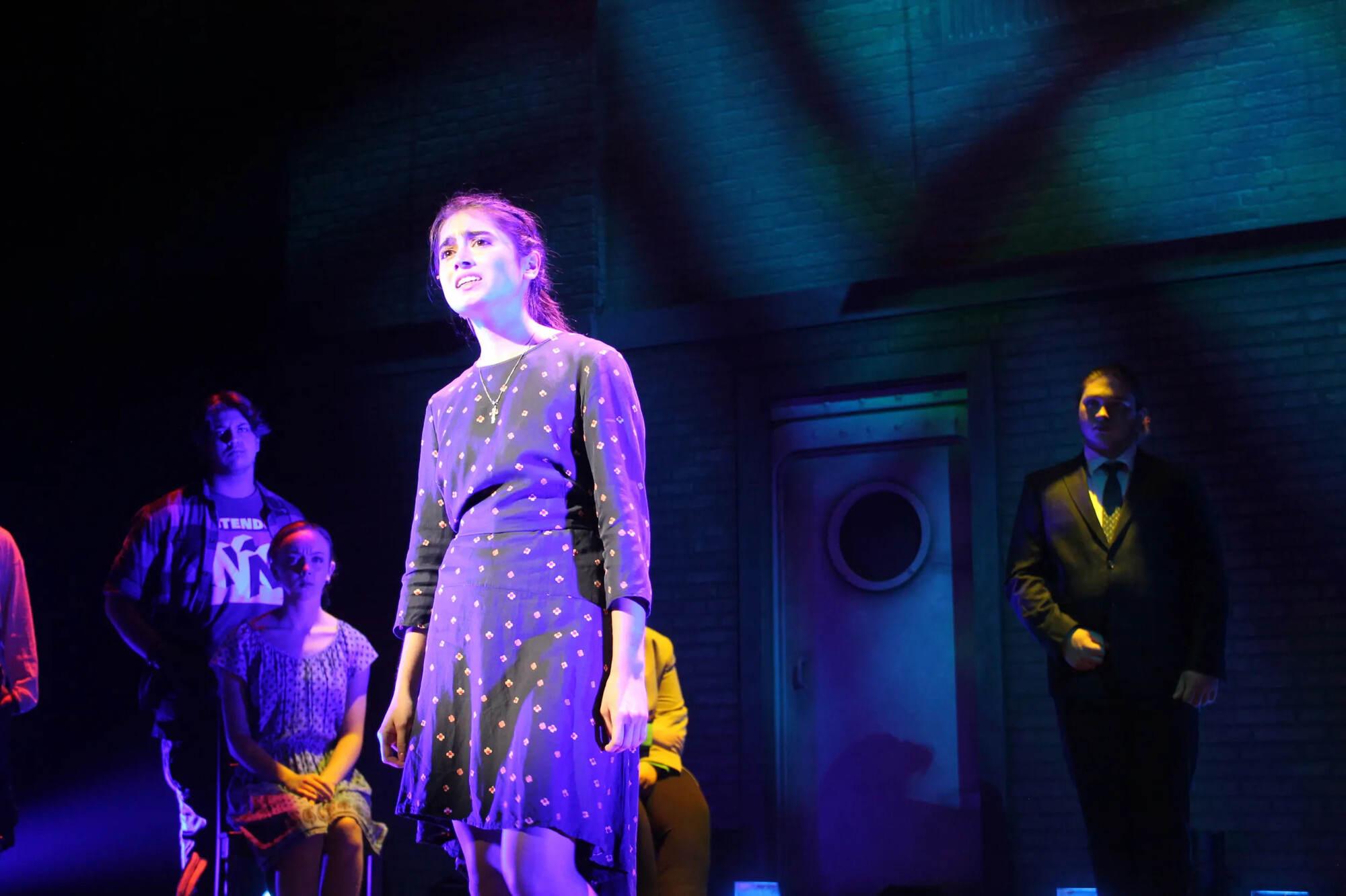 A performer in a polka dot dress stands onstage.