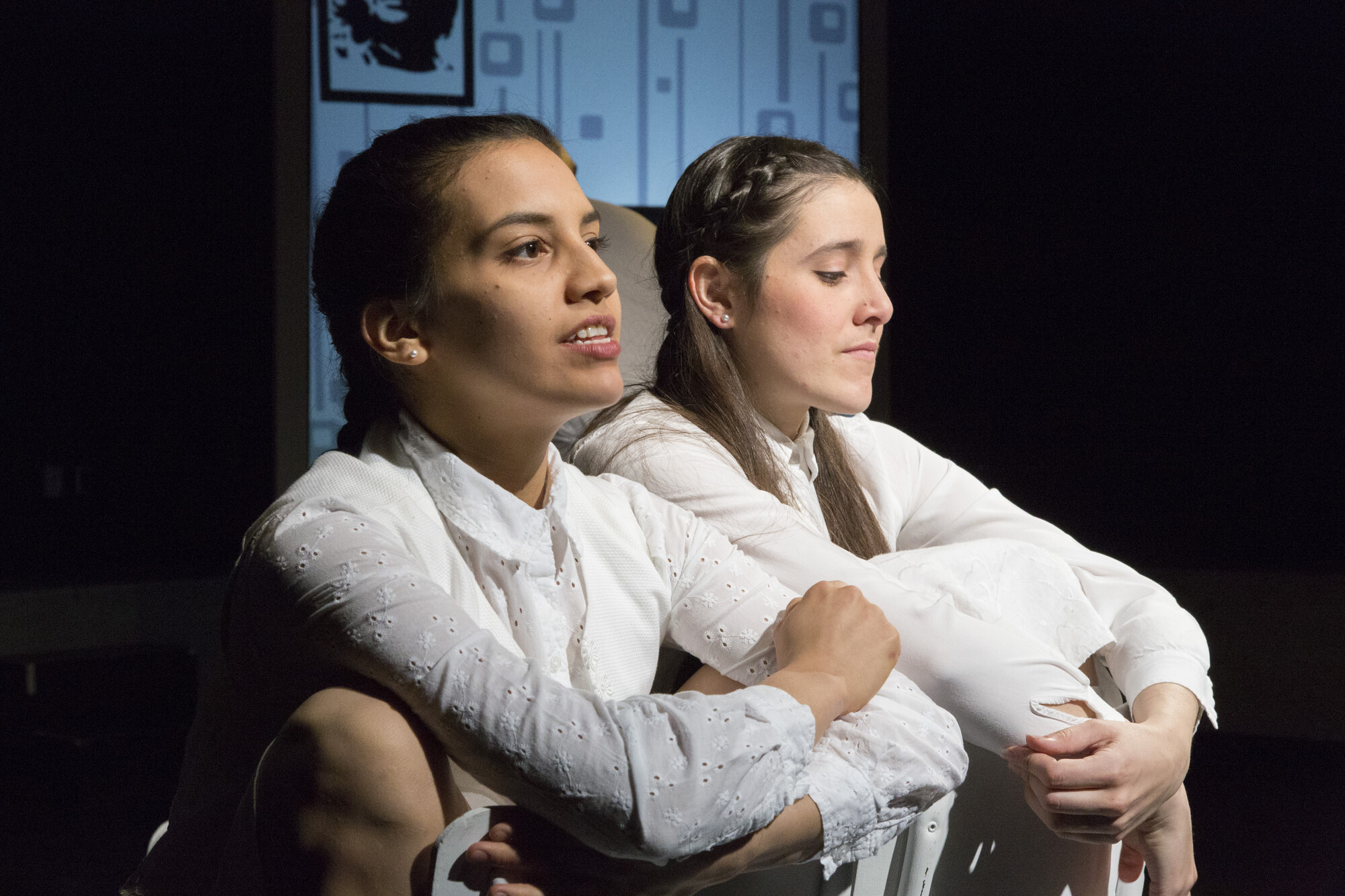 Two women in white dresses kneel onstage.