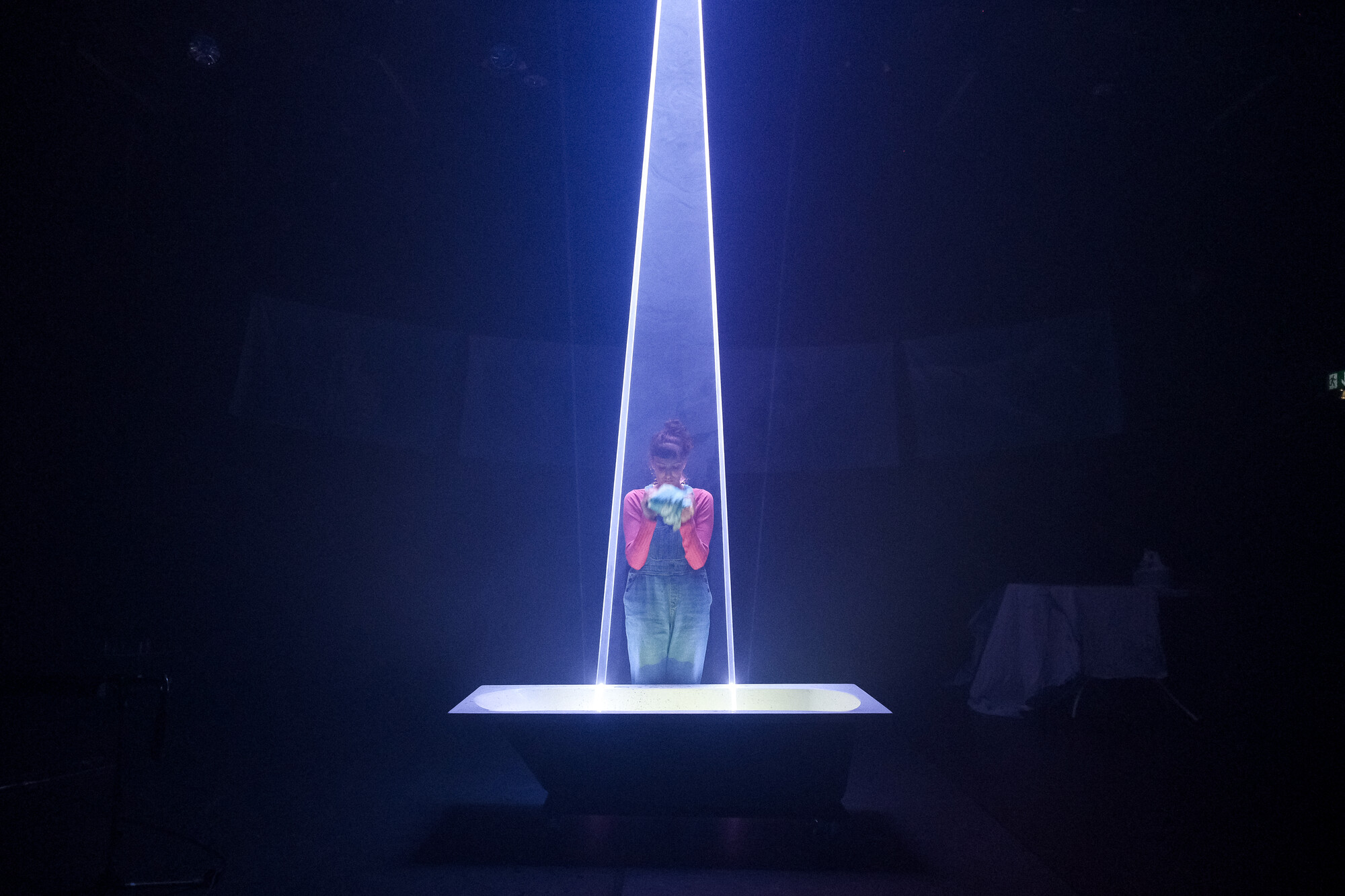 A person stands at a lit table onstage.