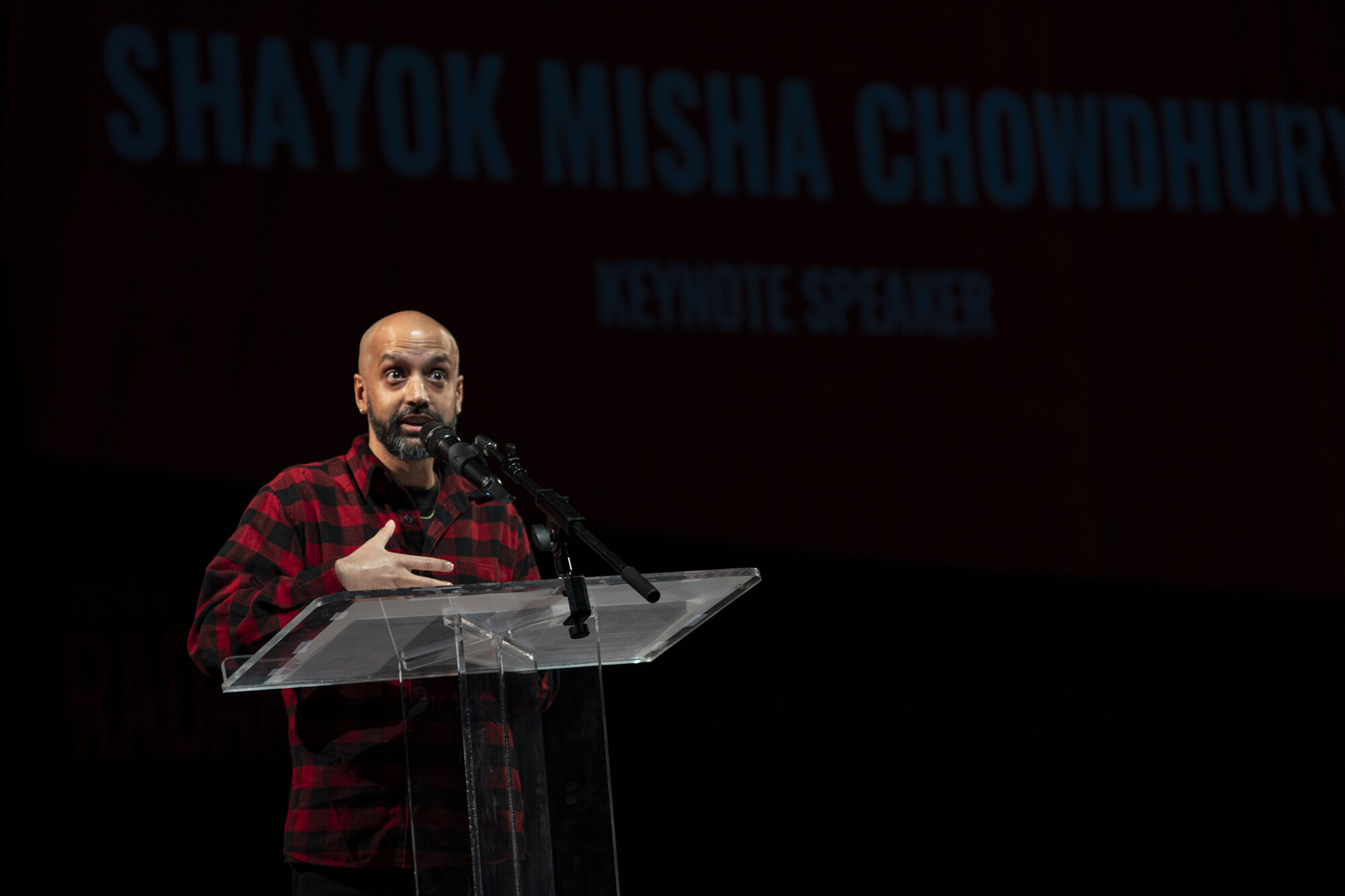 A person in a red flannel speaks onstage.