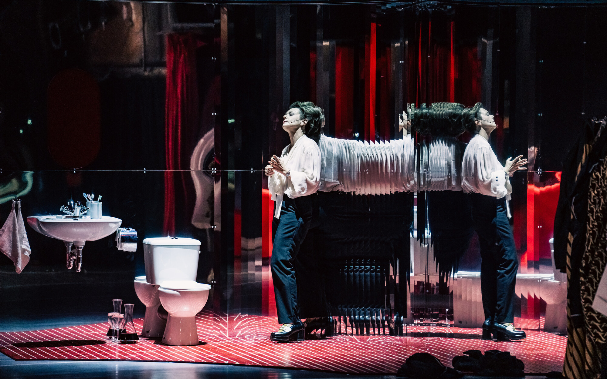 A person stands onstage in front of a series of mirrors.