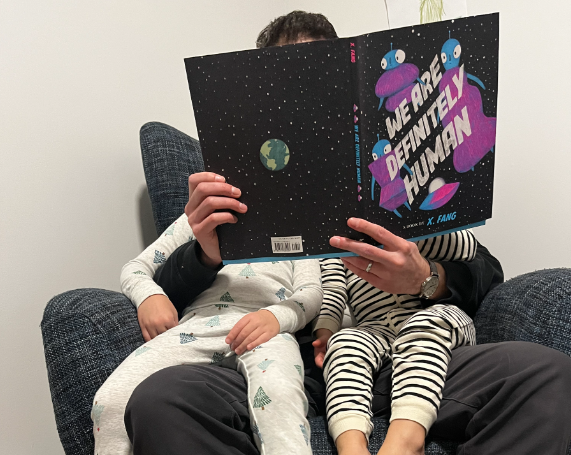 A man reads to two children on his lap.