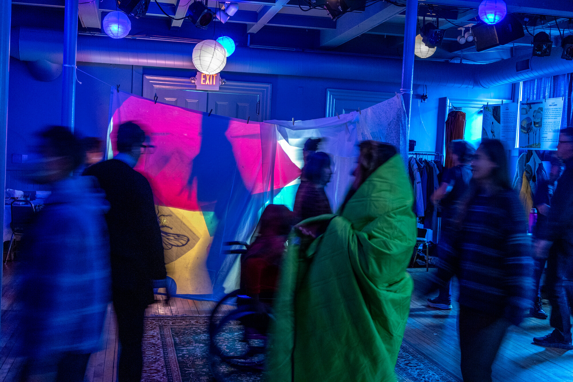 Blurred figures walk around a projection screen.