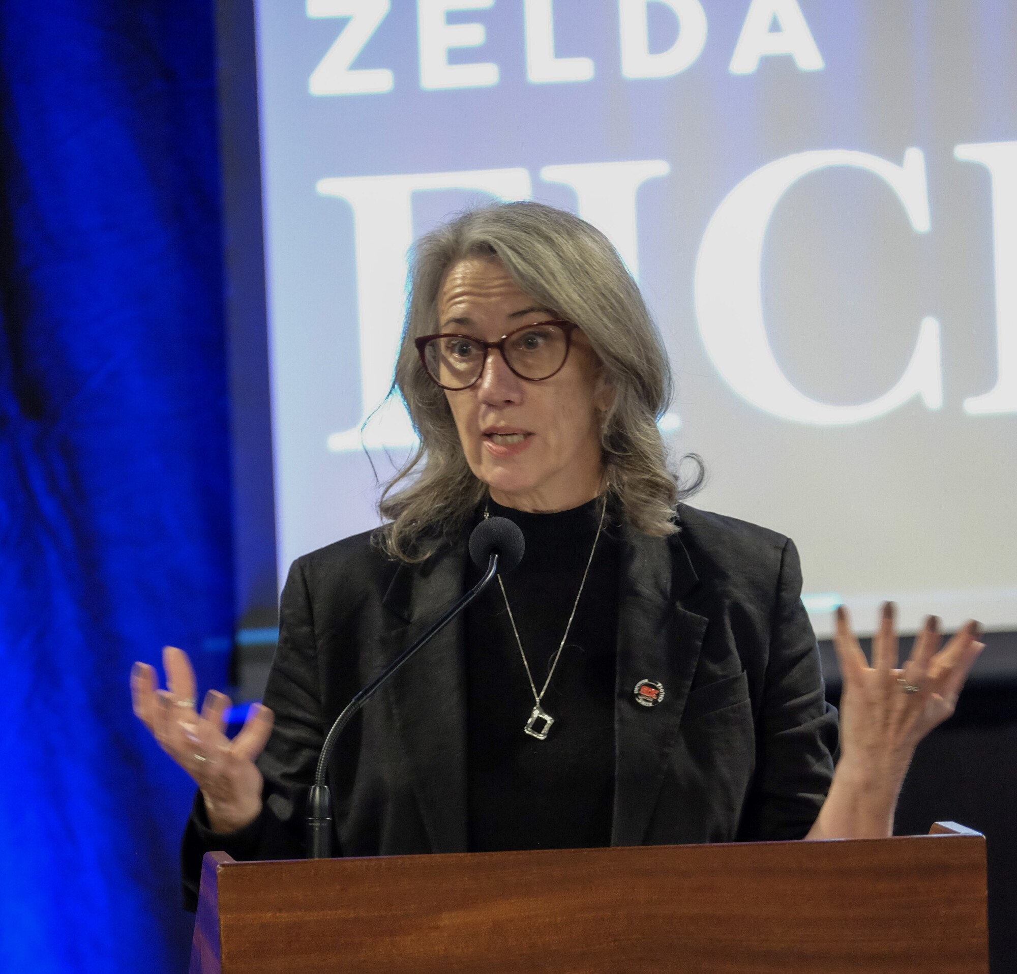 A woman in a blazer speaks at a podium.