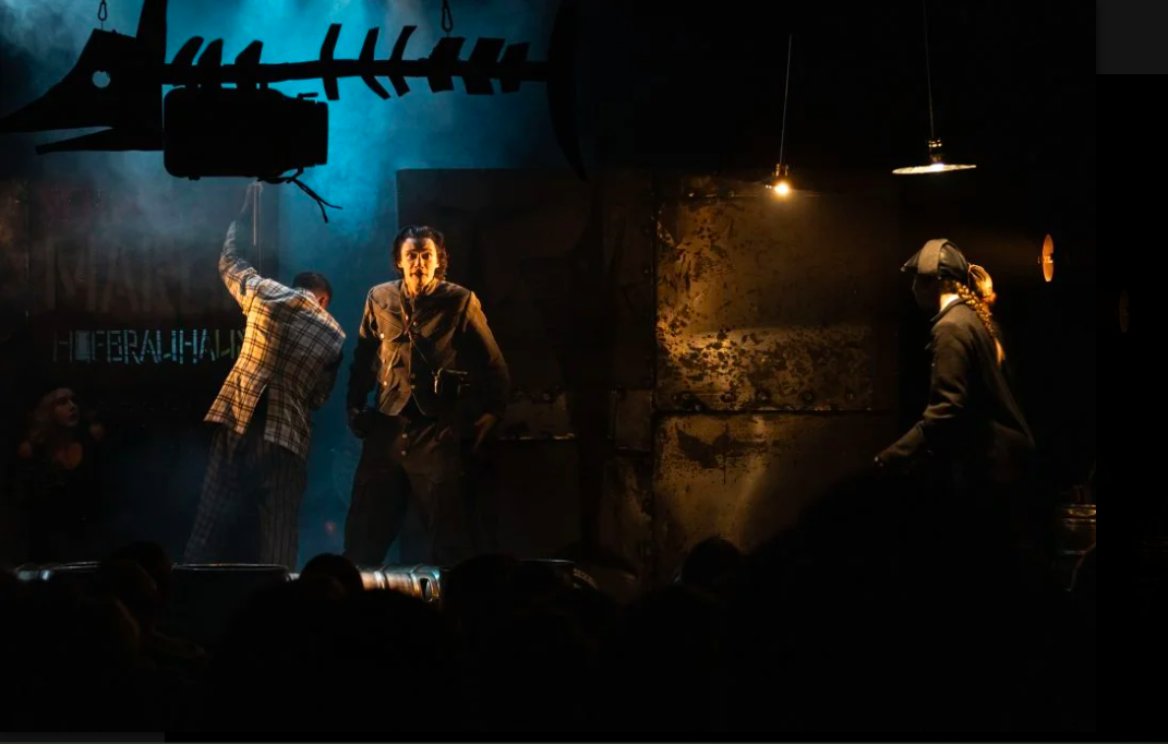 A group of people perform in a dimly lit space onstage.
