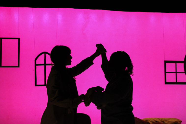 Two actors move in silhouette onstage.