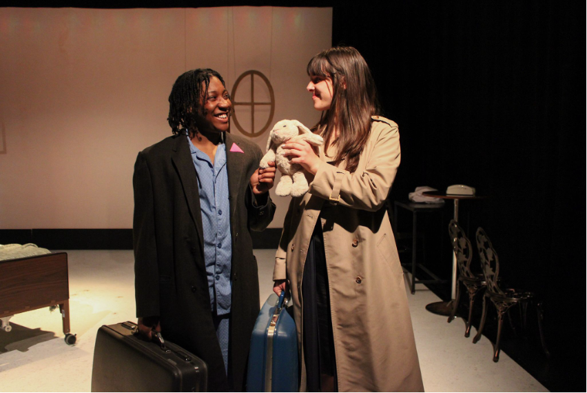 Two people holding suitcases onstage.