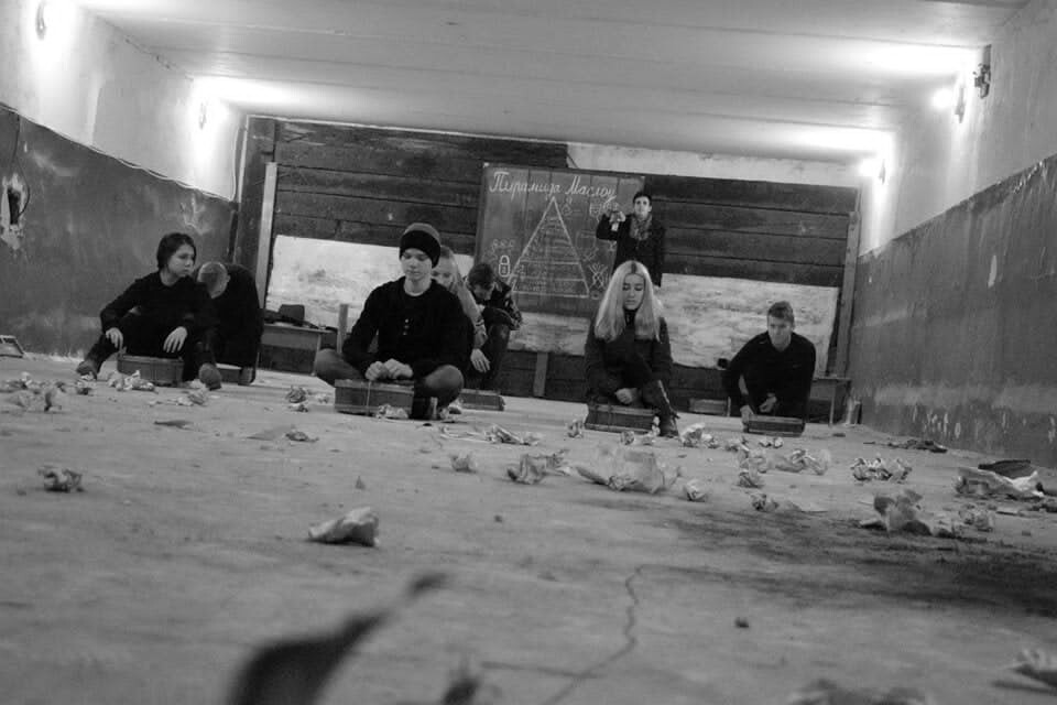 A black and white photo of young people sitting on the floor in a classroom.