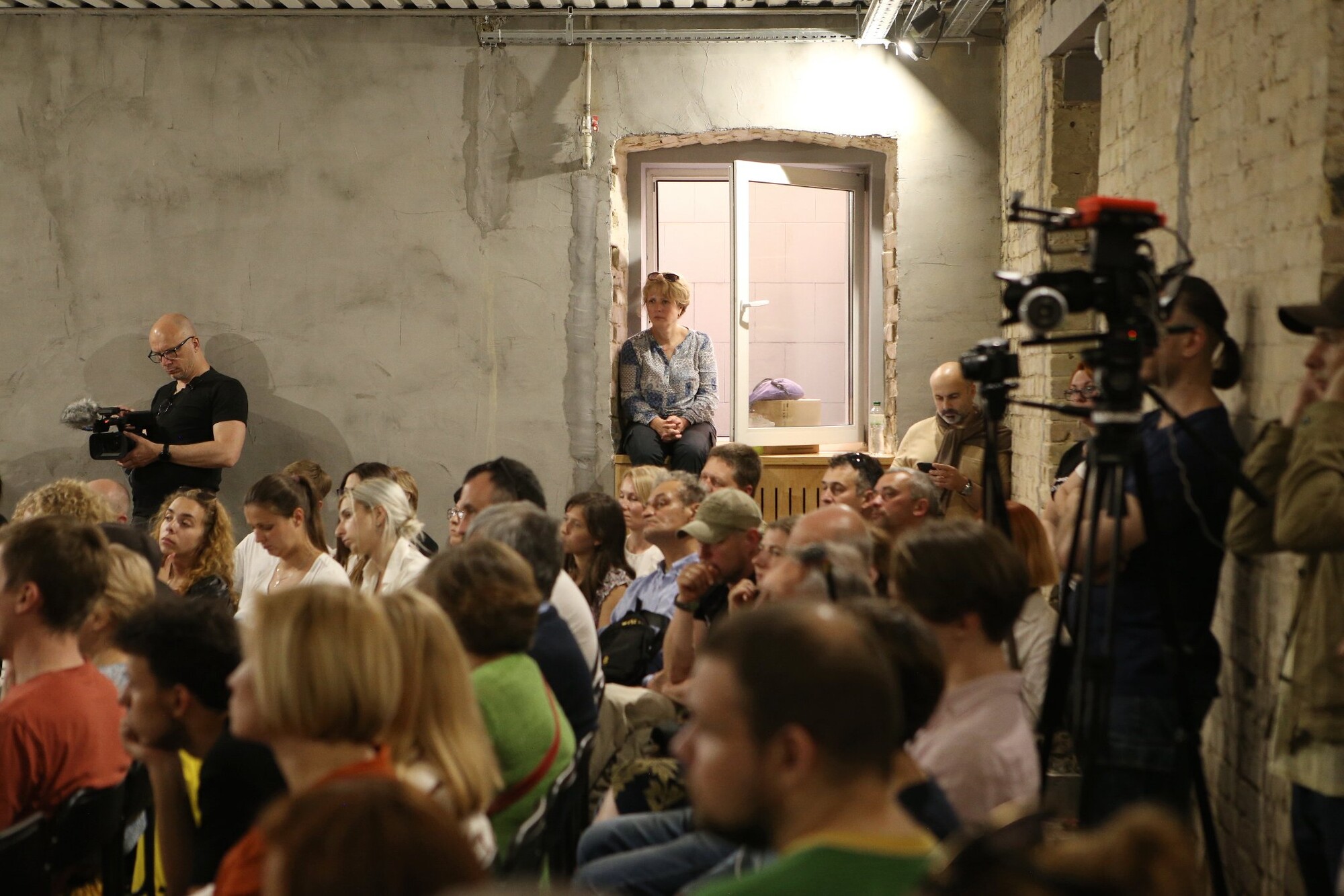 A person sits on a windowsill in a crowded performance space.