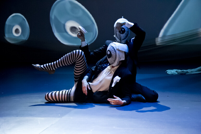Two people dance onstage wearing eyeball masks.