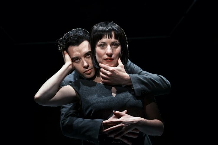 Two people facing forwards while in an embrace and dressed in all black.