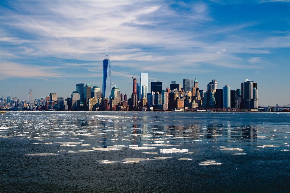 The skyline of New York City on a partly cloudy day as seen from across an icy river.
