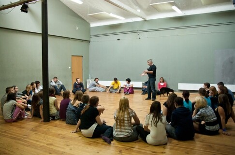 A group of actors sit in a circle during a rehearsal.