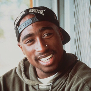 Tupac Shakur smiling and looking at something out of frame.