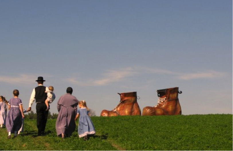 A group of people in prairie clothes walking in a green space towards large shoes.