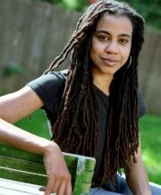 Portrait of Suzan-Lori Parks smiling and leaning an arm against the bench she sits on.