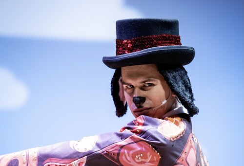A student dressed as a dog in a hat smizes into the camera